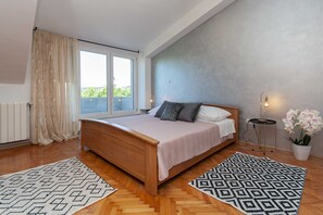 Ein Schlafzimmer mit einem hölzernen Bett, einem großen Fenster, einer Heizung und einer Topf-Orchidee.