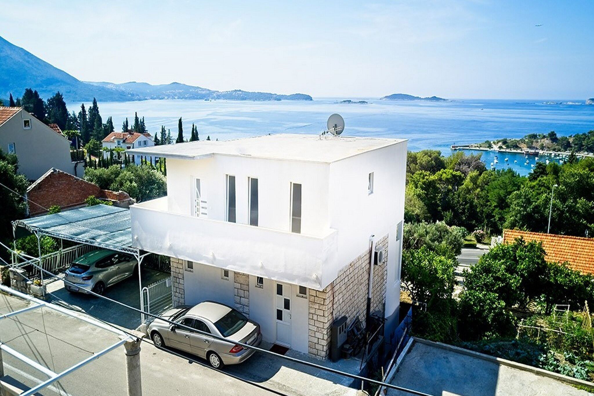 A modern white building with a carport, a satellite dish, and a view of a lake and mountains.