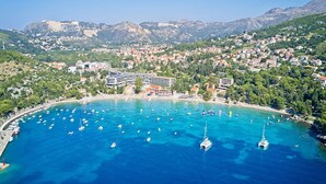 A coastal town with a marina filled with boats, a prominent hotel with a modern design, and a backdrop of mountains. - Apartments Grljević - Studio Apartment with Sea View and Balcony (A2) (Mlini)
