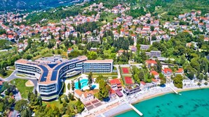 An aerial view of a coastal town with a large, modern hotel featuring a curved design, a swimming pool, and a tennis court. - Apartments Grljević - Studio Apartment with Sea View and Balcony (A2) (Mlini)