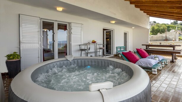 Un jacuzzi con asientos, un patio con mesas y sillas, y vistas del paisaje circundante.