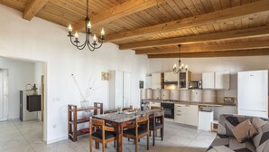 Una cocina moderna con vigas de madera, un área de comedor con una mesa y sillas de madera, y un sofá con estampado geométrico.