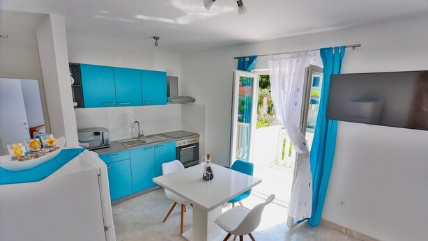 Una cocina compacta con armarios azules, un comedor con mesa blanca y un televisor de pantalla plana.