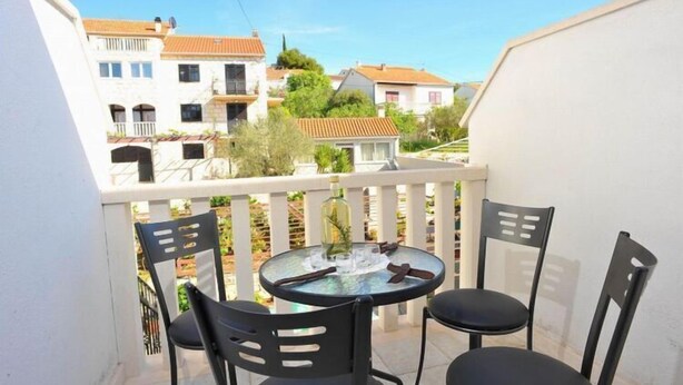 Un balcón con una mesa redonda y cuatro sillas, con vista a una zona residencial con casas y vegetación.