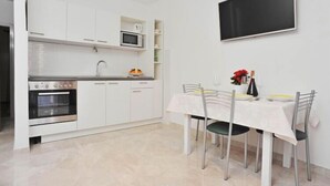 Una cocina moderna con armarios blancos, un microondas y un horno. Hay una mesa de comedor con sillas y un televisor de pantalla plana montado en la pared.