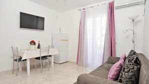 Una sala de estar con sofá, una mesa de comedor con sillas, un televisor de pantalla plana montado en la pared y un refrigerador.