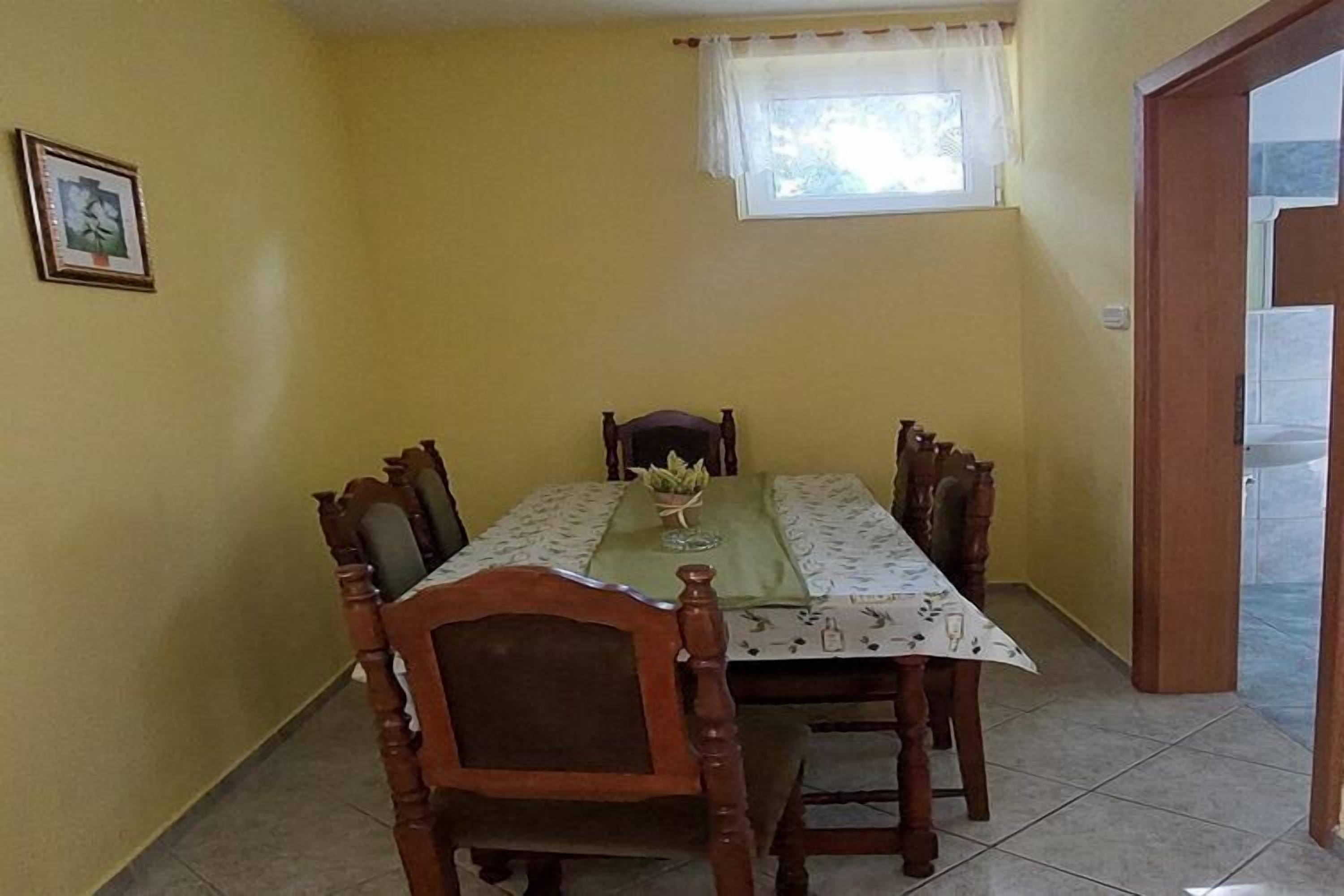 Een eetruimte met een tafel en stoelen, een raam met gordijn en een deur naar een andere kamer.