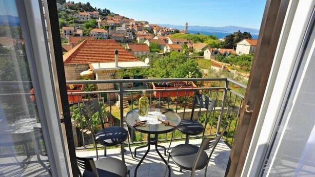 A balcony with a table and chairs, overlooking a town with red-roofed buildings and a clear view of the sea. - Apartments Lenka - One Bedroom Apartment with Balcony and Center View A3 (Sutivan)
