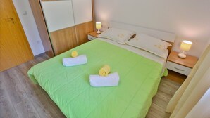 A neatly made bed with green bedding, two bedside lamps, and rolled towels on the bed. - Apartments Lenka - Two Bedroom Apartment with Garden Terrace A4 (Sutivan)