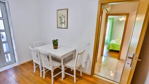 A room with a white table and four chairs, a framed picture on the wall, and a door leading to a bedroom with a green bedspread. - Apartments Lenka - Two Bedroom Apartment with Garden Terrace A4 (Sutivan)