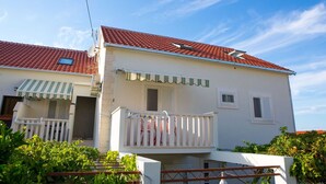 A two-story house with a red-tiled roof, a balcony with a white railing, and a satellite dish. - Apartments Lenka - Two Bedroom Apartment with Garden Terrace A4 (Sutivan)