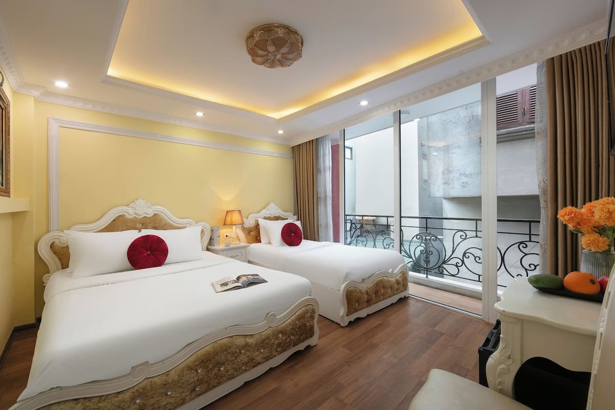 A hotel room with two beds, a balcony with a view, and a small table with a vase of flowers.