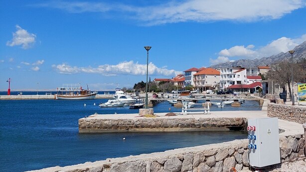 Un puerto deportivo con barcos amarrados, un muro de piedra y edificios con tejados rojos al fondo.