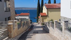 Una calle estrecha con paredes de piedra y techos de tejas rojas, que conduce a vistas del mar.