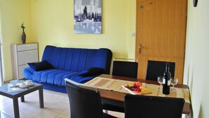 Una sala de estar con un sofá azul, una mesa de comedor con una botella de vino y un cuadro en la pared.