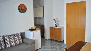 Un espace de vie compact comprenant un coin cuisine, un canapé avec des coussins à rayures et une porte en bois.