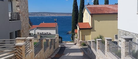 Une rue étroite, bordée de murs de pierre et surmontée de toits couverts de tuiles rouges, qui mène à un point de vue sur la mer.