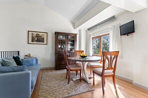 Un salon comprenant un canapé, une table à manger, des chaises, un meuble, un téléviseur et une fenêtre avec des rideaux.