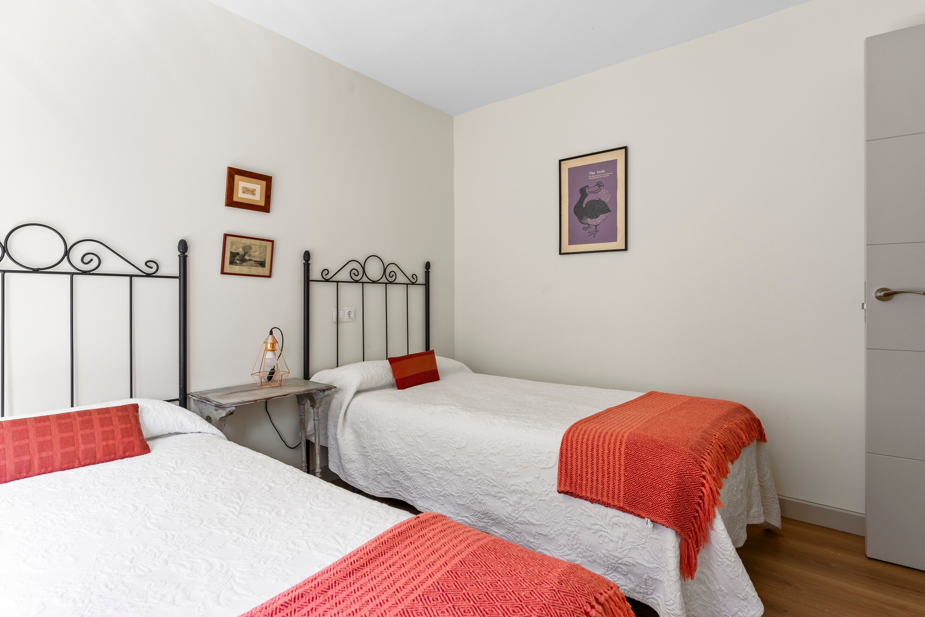 Una habitación con tres camas individuales, una mesita y una puerta.