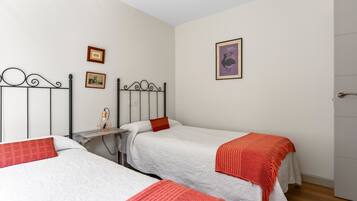 Una habitación con tres camas individuales, una mesita y una puerta.
