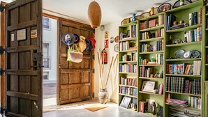 Una habitación con una puerta de madera, una estantería verde llena de libros, una cesta de mimbre y un jarrón con cañas.