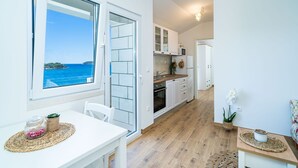 A modern kitchen with white cabinets, a wooden countertop, and a view of the sea through a large window.