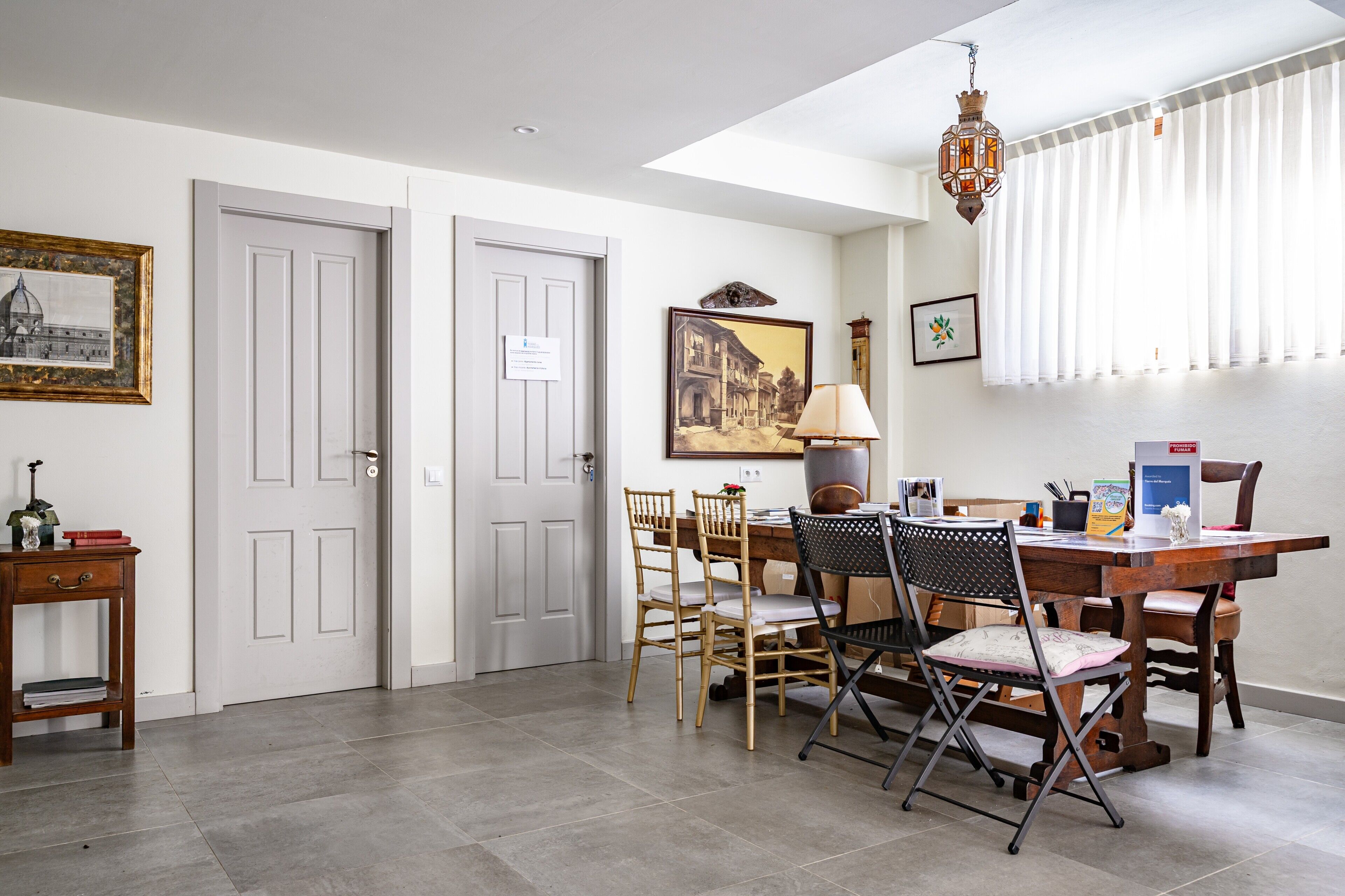 A dining area with a wooden table, chairs, a lamp, and framed pictures on the wall.