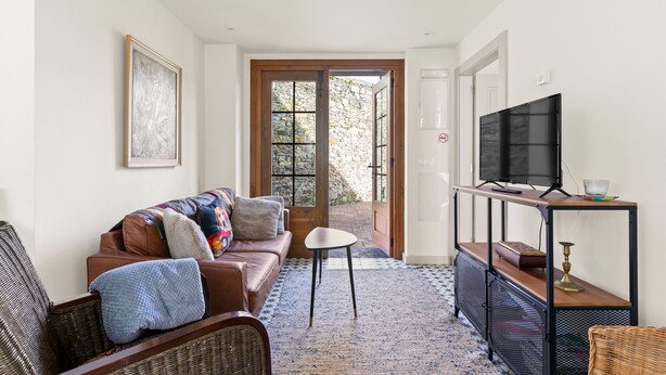 Una sala de estar con un sofá, un televisor sobre un mueble bajo, una mesita y una puerta que da al exterior.