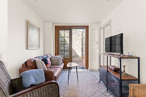 Un salon avec un canapé, un téléviseur posé sur un meuble, une petite table et une porte donnant sur l’extérieur.