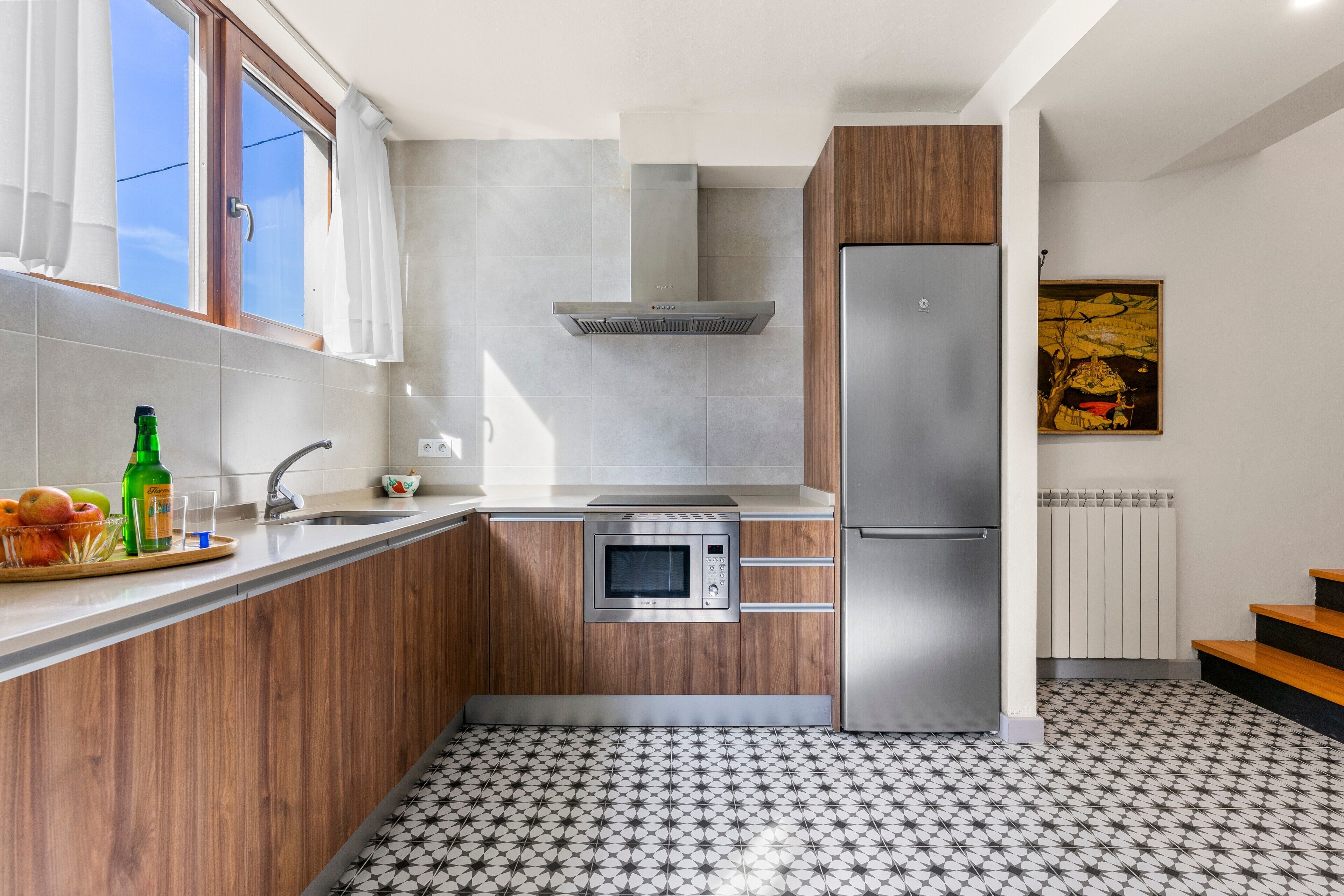 Een moderne keuken met een magnetron, een koelkast van roestvrij staal en houten keukenkastjes.