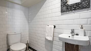 Une salle de bain avec des carreaux de céramique blancs rectangulaires, des toilettes, un lavabo et une serviette accrochée au mur.