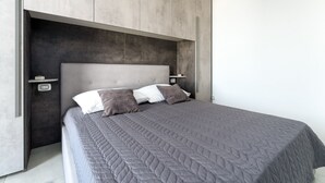 Une chambre moderne avec un grand lit, une literie grise et une tête de lit intégrée.