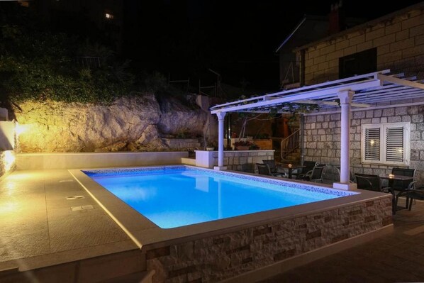 Uma piscina com pérgula branca, paredes de pedra e área de estar ao ar livre.