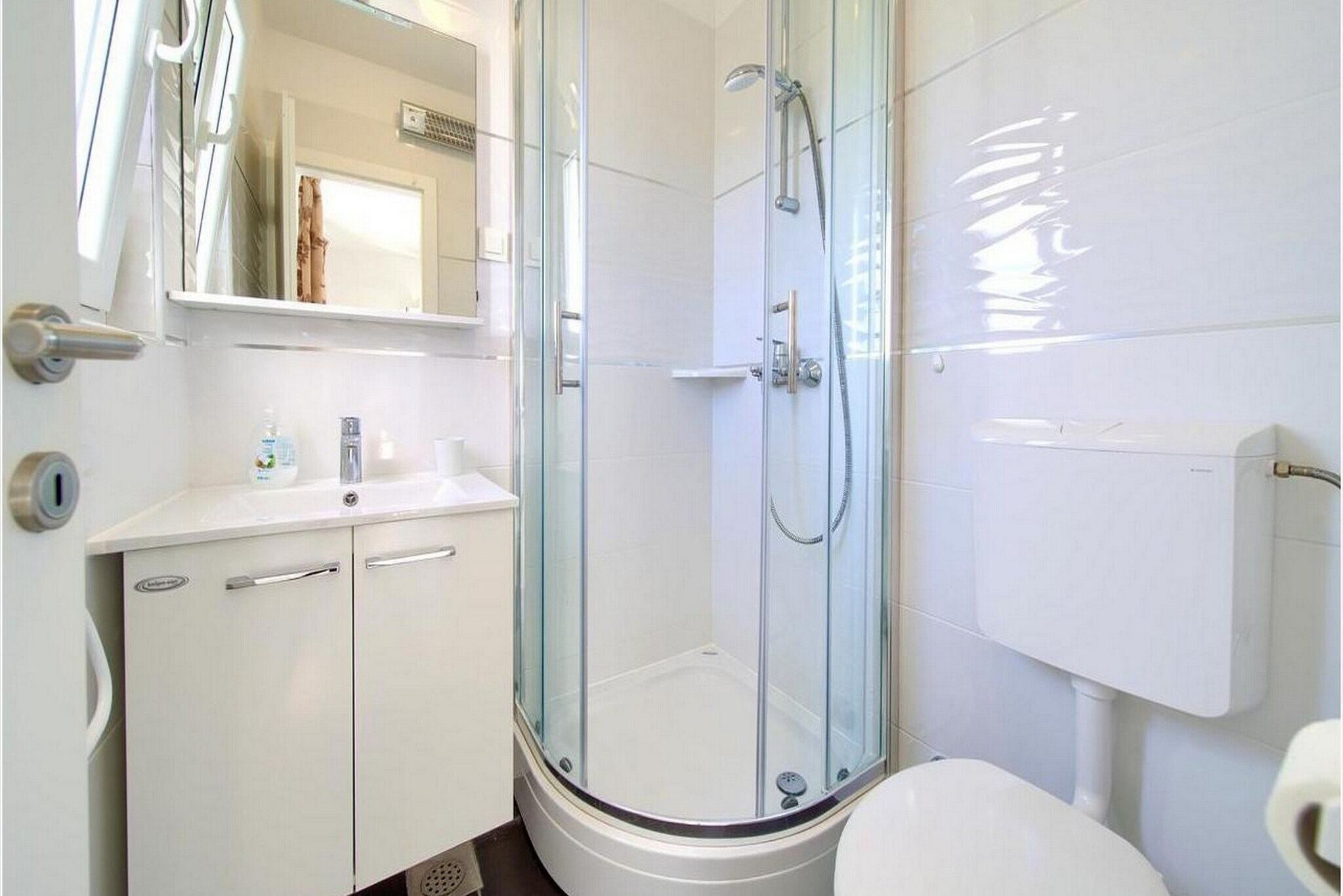 Une salle de bain moderne avec une douche à parois de verre, un lavabo blanc avec un miroir et des toilettes.