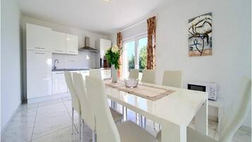 A modern kitchen with white cabinets, a dining table with chairs, and a microwave on a side table.