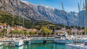 Una marina con imbarcazioni ormeggiate, circondata da edifici e montagne.