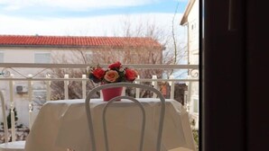 A balcony with a table and chairs, a potted plant with flowers, and a view of a building with a red roof.