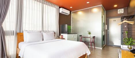 A modern hotel room with a large bed, a desk, a chair, and a small table with a plant.