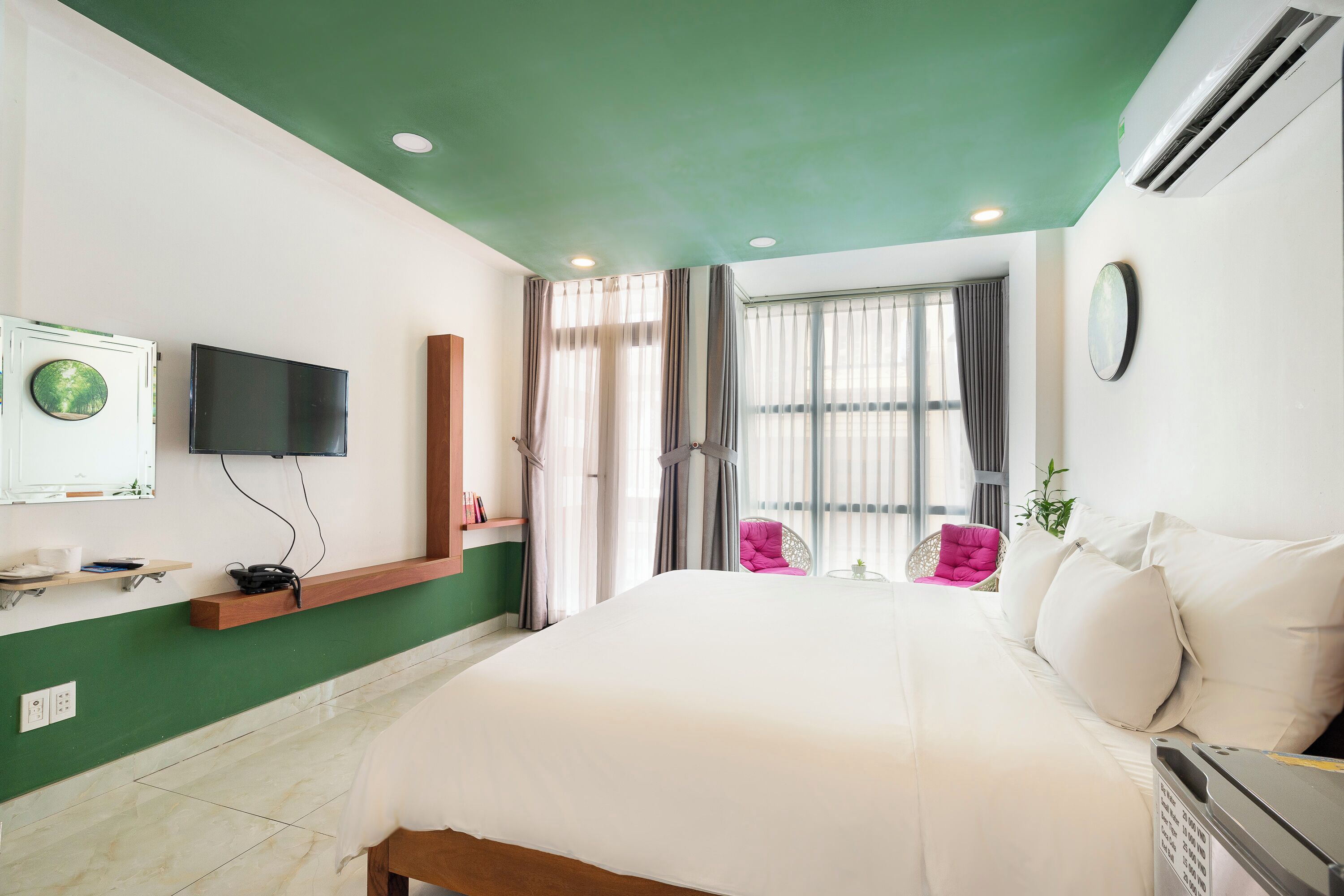 Een hotelkamer met een bed, een aan de muur bevestigde televisie, een raam met gordijnen, een tafeltje en een stoel.