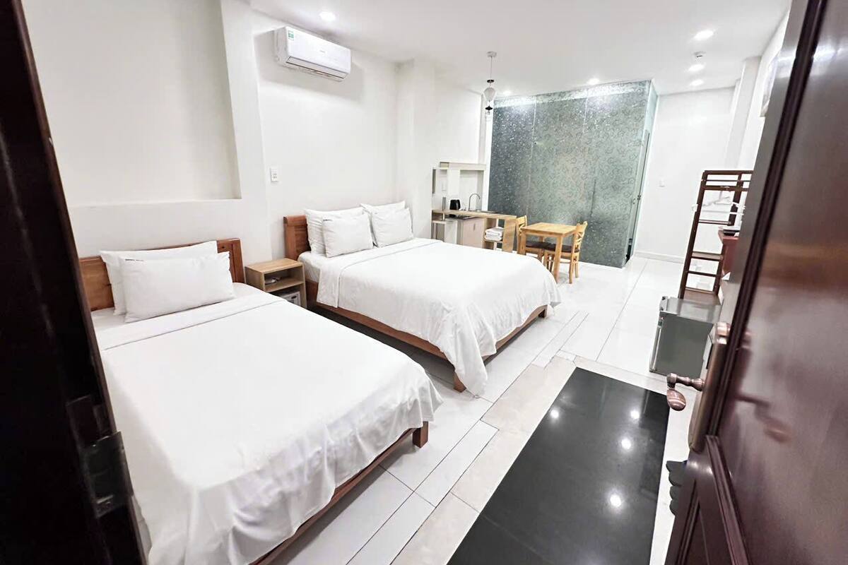 Une chambre d’hôtel avec deux lits, un bureau, une chaise, une petite table, un appareil de climatisation et une salle de bain avec douche et toilettes.
