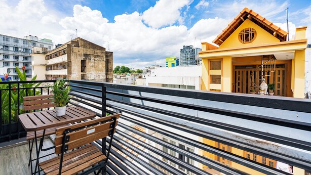 Een balkon met een houten tafel en bank, met uitzicht op een stadsgezicht met verschillende gebouwen.