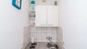 Una kitchenette pequeña con un lavamanos, dos grifos, una estufa y un reloj en la pared.