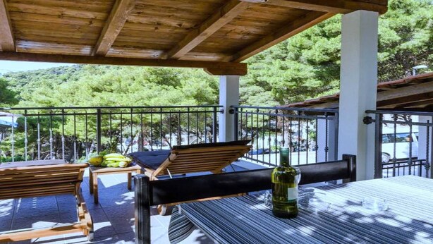 Un espacio de estar al aire libre techado con mobiliario de madera y una mesa con una botella.
