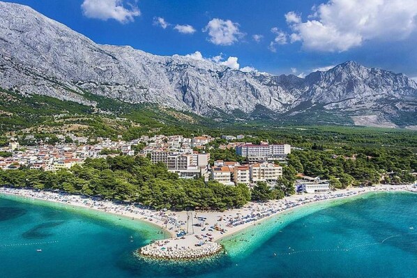 A coastal town with a beach, buildings, and mountains in the background.