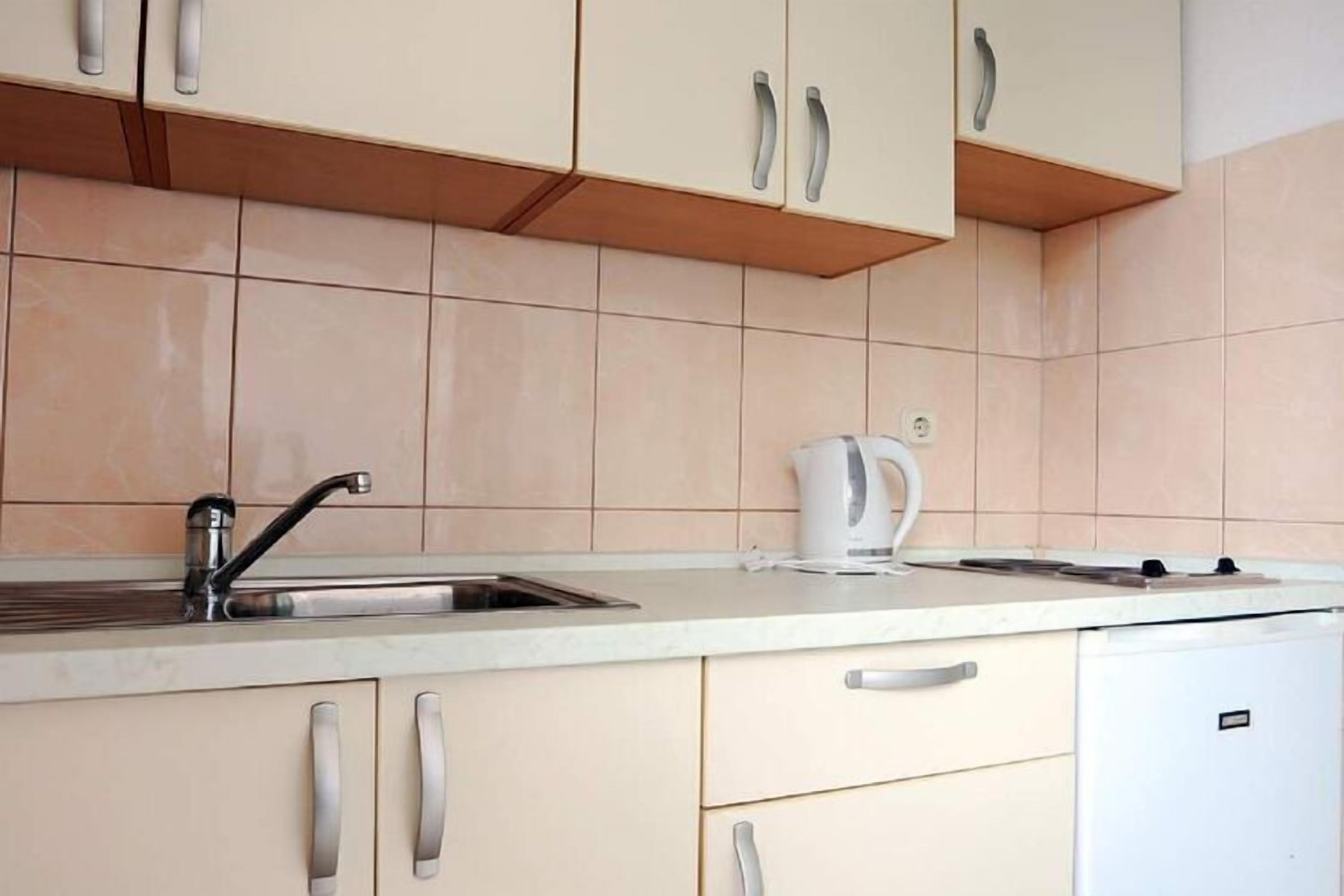 Una cocina con gabinetes color crema, un fregadero de acero inoxidable y un hervidor blanco.