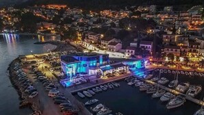 Ein Hotel direkt am Wasserufer mit einer Marina, das ein modernes Gebäude mit blauer Beleuchtung, einen Parkplatz und angestellte Boote zeigt.