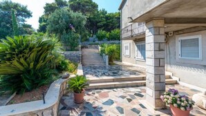 Un chemin de pierres menant à un bâtiment doté d’un balcon, entouré d’une végétation luxuriante et de plantes en pot.
