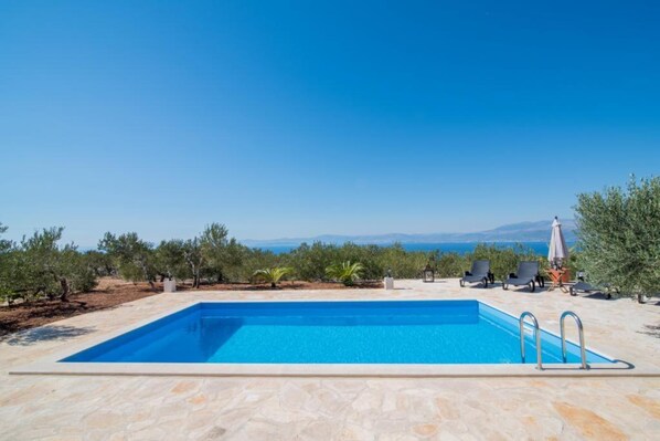 Ein rechteckiger Pool mit klarem, blauem Wasser, umgeben von Steinplatten und mit Blick auf eine malerische Landschaft mit Bäumen und fernen Bergen.