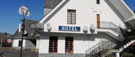 Un bâtiment blanc avec une enseigne bleue sur laquelle on peut lire « HÔTEL », et un escalier menant à un balcon.