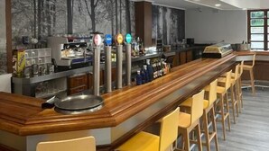Un espace bar moderne avec un long comptoir en bois, de nombreux tabourets et une fresque représentant des arbres sur le mur.